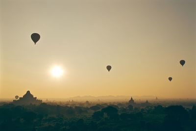 Hot air balloons over temples in city against clear sky during sunset