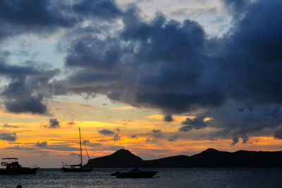 Silhouette sailboats in sea against dramatic sky during sunset