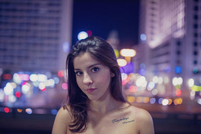 Portrait of young woman at illuminated city