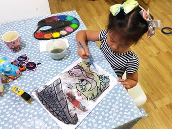 High angle view of girl painting on paper at home