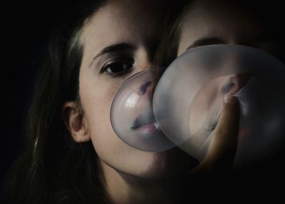 Double exposure of woman blowing bubble against black background