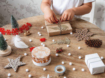 Child wrapped christmas presents in craft paper with decoration. wooden table with new year gifts.