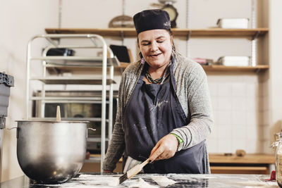 Mature female baker making dough using scrapper on kitchen counter