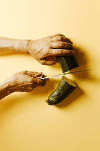 Cropped hands of woman cutting cucumber over beige background