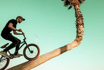 Low angle view of man riding bicycle on tree trunk against clear sky