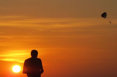 Rear view of silhouette man standing against orange sky at sunset