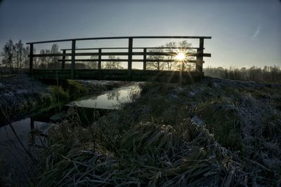 Footbridge over river against sky in forest during winter