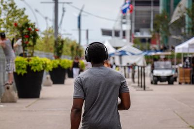 Rear view of young man listening music while walking on city street