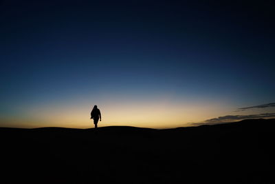 Silhouette man standing on mountain against clear sky during sunset