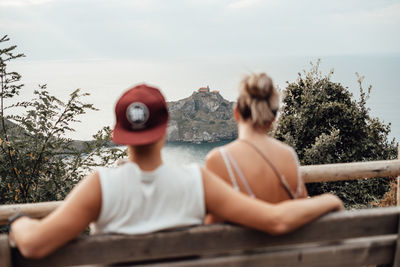 Rear view of young couple sitting on bench against sea