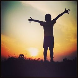 Silhouette of woman with arms raised at sunset