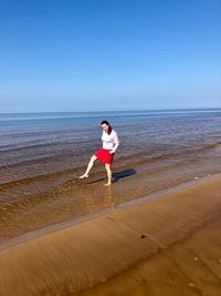Full length of woman standing on shore at beach against blue sky
