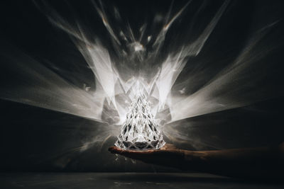 Cropped hand of person holding crystal in darkroom