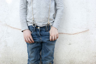 Boy with snap hook suspenders standing in front of wall