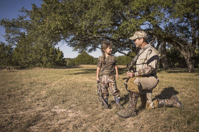 Father and daughter holding archery bows on grassy field