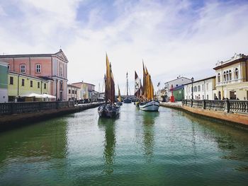 Sailboats in canal amidst buildings against sky