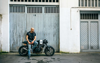 Man with motorcycle against wall in city