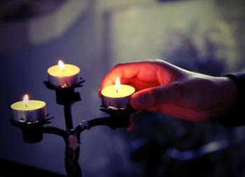 Close-up of cropped hand holding lit tea light candle in temple