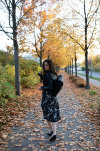 Portrait of woman holding flower while standing by trees during autumn