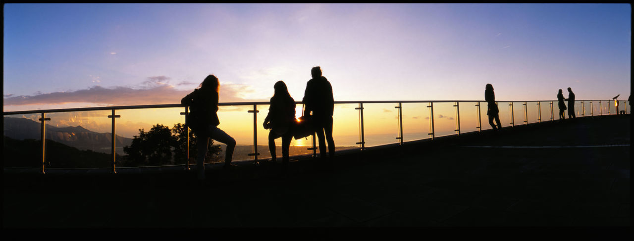 SILHOUETTE PEOPLE STANDING ON RAILING DURING SUNSET