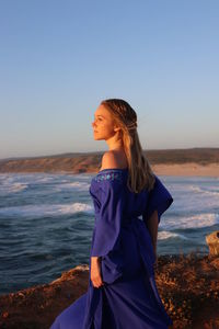 Woman standing at beach against blue sky