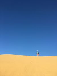 Man on sand dune against clear blue sky