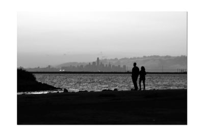 Silhouette people standing on sea shore against sky