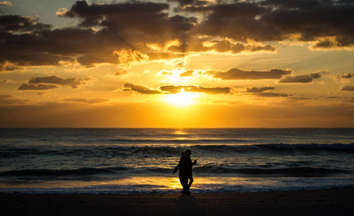 Silhouette people standing on beach against sky during sunset