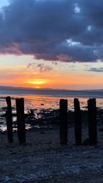 Wooden posts on beach against sky during sunset