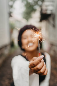 Smiling woman holding lit sparkler in city