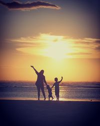 Silhouette family enjoying at beach against sky during sunset