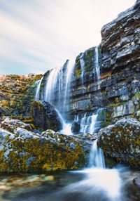 Low angle view of waterfall against cloudy sky