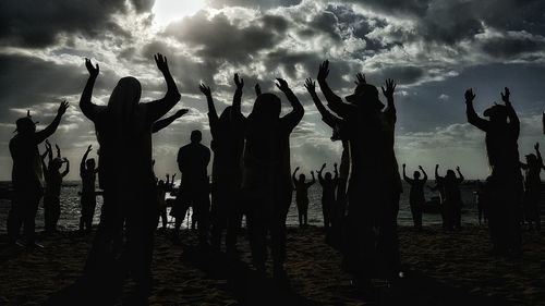 Silhouette people with arms raised standing at beach