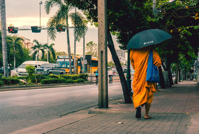 Rear view of man with umbrella walking on street during rainy season