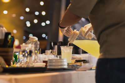 Man pouring juice from jar into a tak away glasses at the shop.