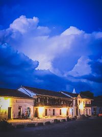 Illuminated buildings by street against sky at night