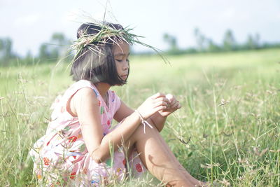 Cute girl wearing grass wreath while sitting on field