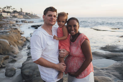 Portrait of happy parents with daughter at beach during sunset