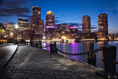 Illuminated city by river against sky at night