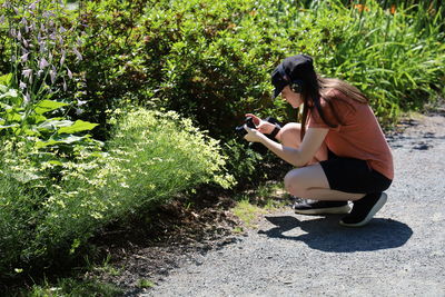 Side view of girl using mobile phone to photograph plants.