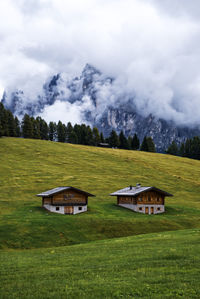 Houses on field against sky and cloudy mountains