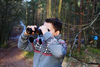 Boy looking through binoculars while standing in forest