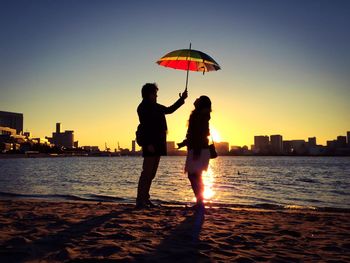 Silhouette man and woman standing under umbrella at beach during sunset