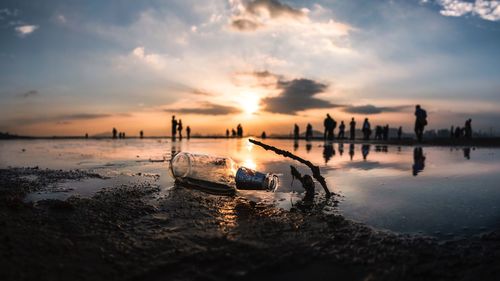 Close-up of empty bottle at beach against sky during sunset