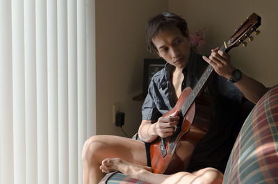 Mid adult man playing guitar while sitting on sofa at home