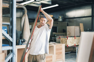 Male carpenter carrying wooden plank at workshop