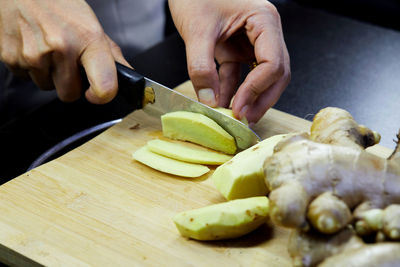 Person slicing peel of ginger root on cutting board by knife