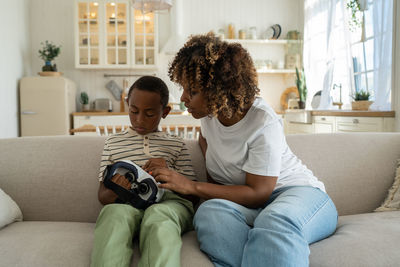 Mother and daughter using laptop while sitting on sofa at home