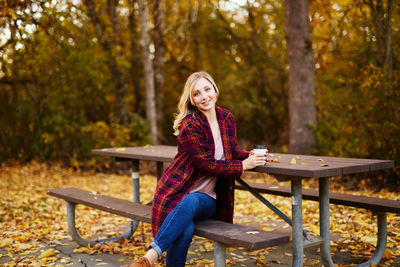 Young woman sitting on picnic table in park during autumn