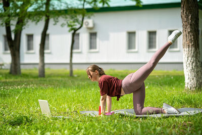 Young girl having online workout outdoors using laptop. pilates or yoga video lesson on internet. 